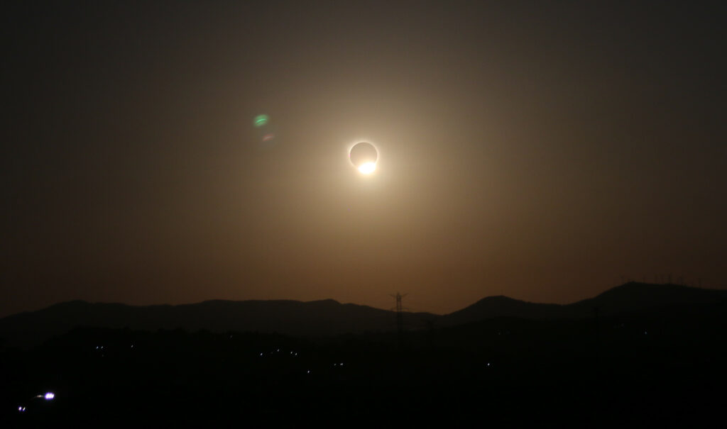 Éclipse du 12 août 2026. Fin de la phase totale, gros plan de l'environnement. Les voitures ont leur phares allumés.